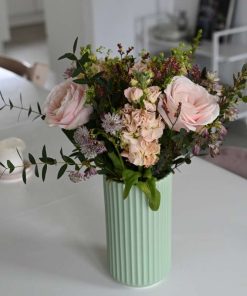 Buket med lyserøde roser, og andre lyserøde blomster som astrantia, limolium, leukøjer og forskelligt grønt på hvidt bord