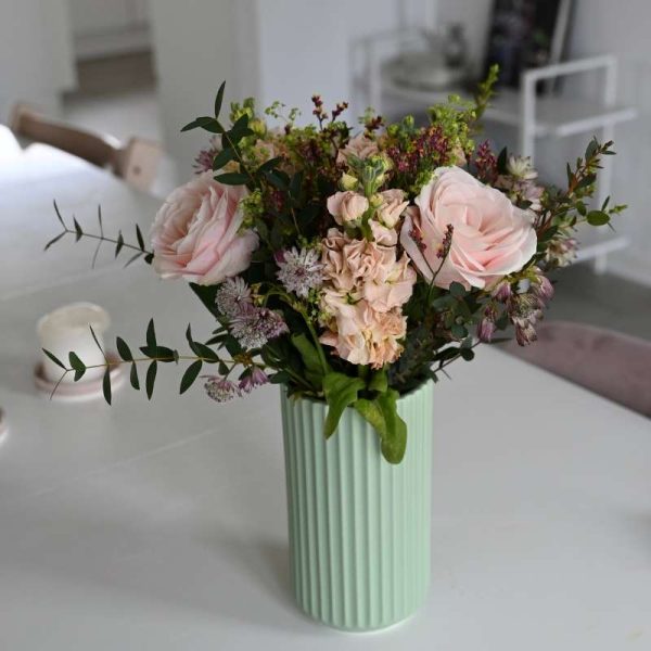 Buket med lyserøde roser, og andre lyserøde blomster som astrantia, limolium, leukøjer og forskelligt grønt på hvidt bord