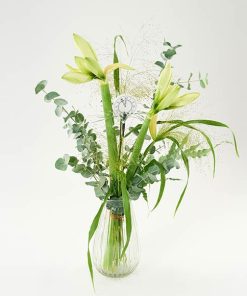 En buket af hvide amaryllis, eucalyptus, græsser og nytårspynt, står i en gennemsigtig vase.