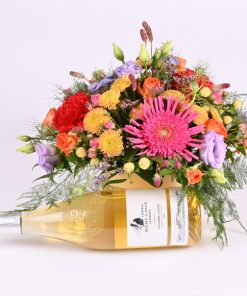 Friske blomster i en rund æske, og foran dekorationen ligger der en flaske vin.