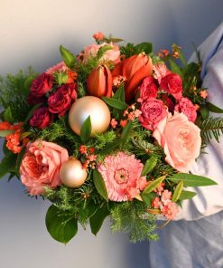 Buket i lyserøfe og røde farver med julekugler og amaryllis holdt i hånden