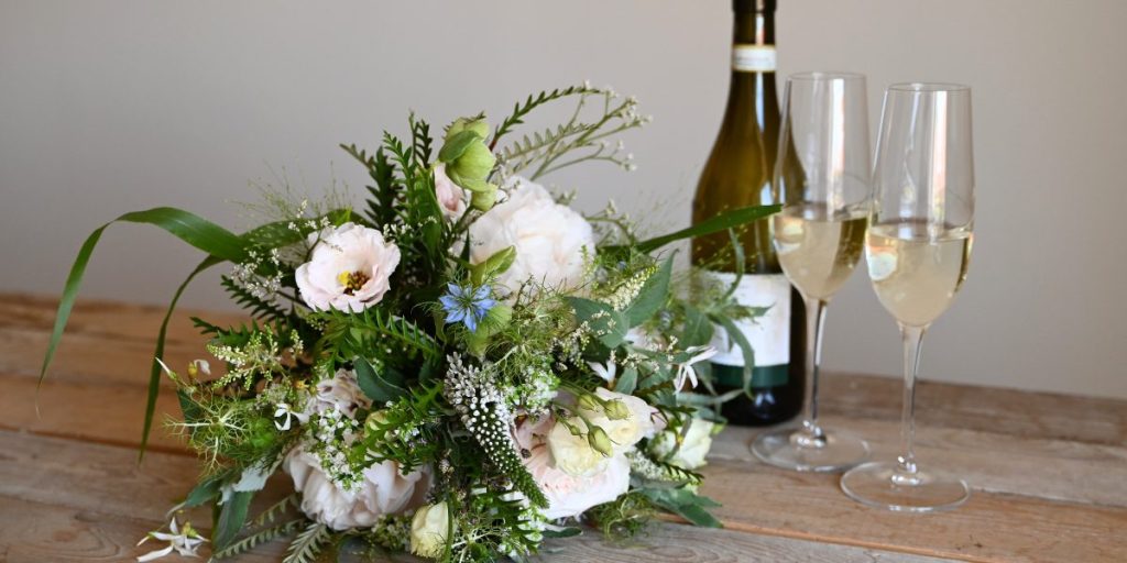 Brudebuket på rå træplade med vin og glas i baggrunden