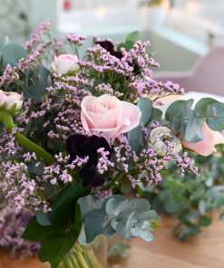 Luftig buket i rosa og lyserøde nuancer, som står i en gennemsigtig glasvase. på et træbord i hjemlige omgivelser.