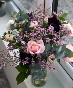 Luftig buket i rosa og lyserøde nuancer, som står i en gennemsigtig glasvase i en vindueskarm.