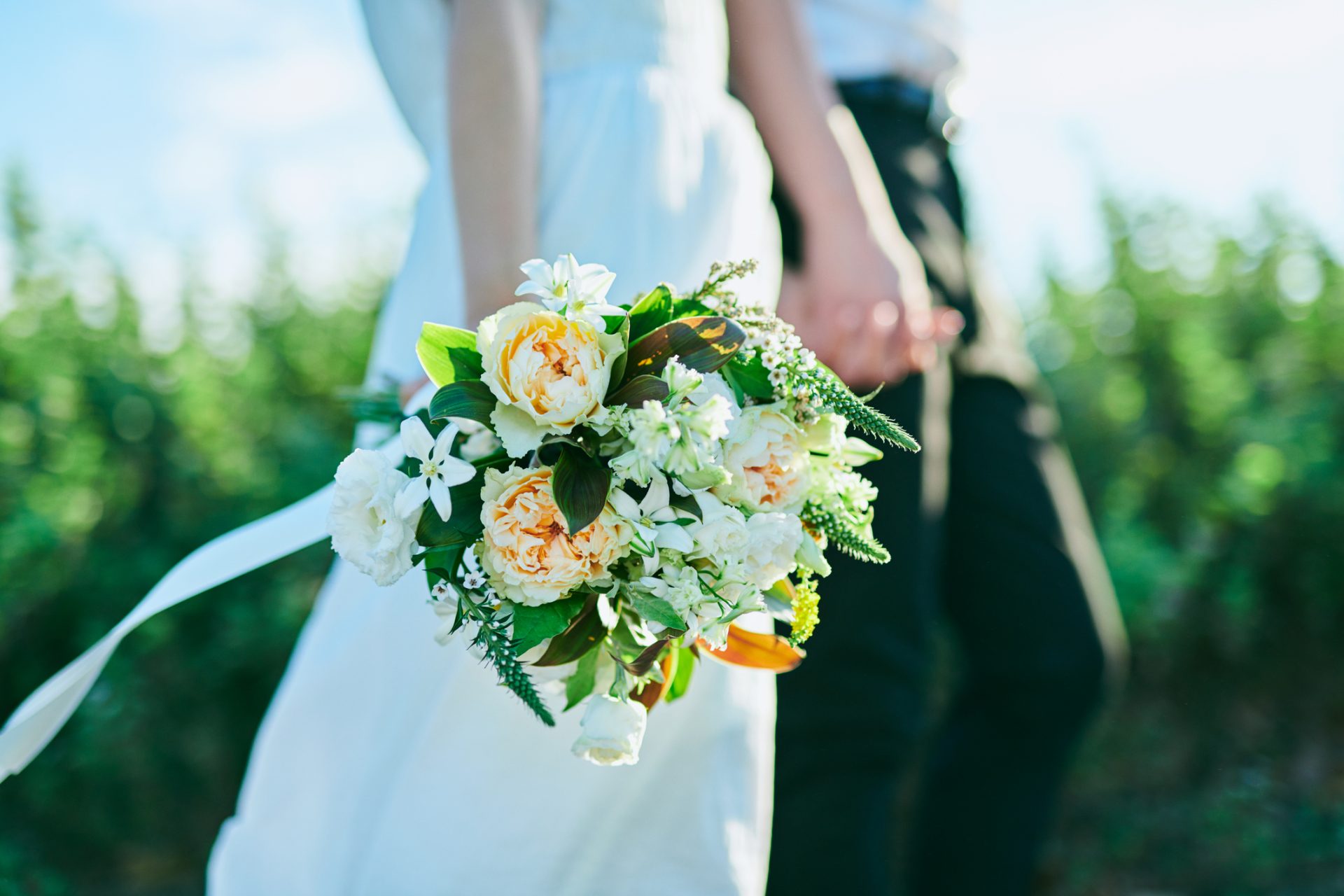 Brudepar går hånd i hånd, og der er fokus på brudebuketten i forgrunden.