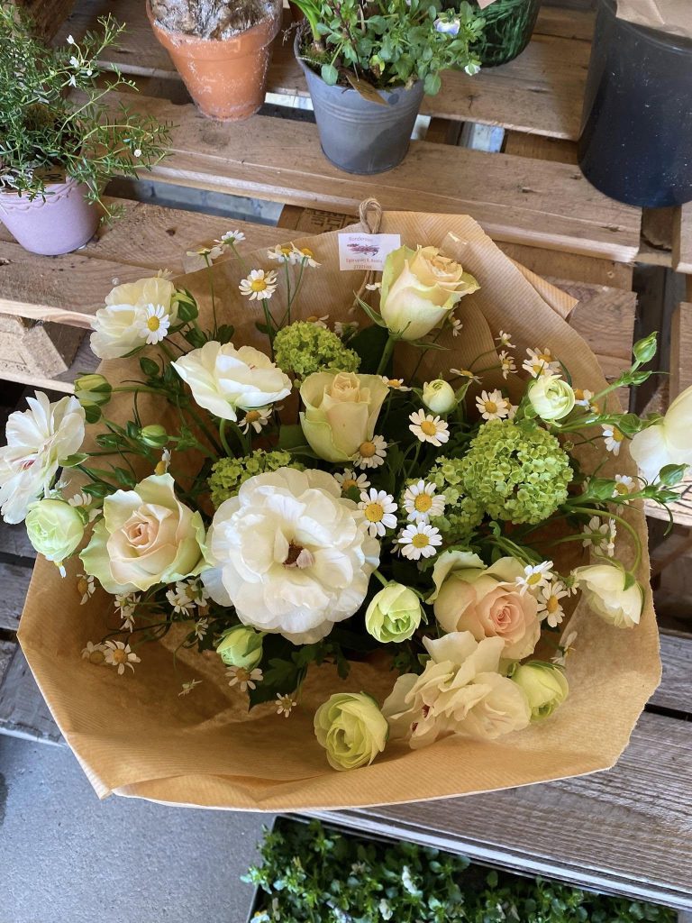 En lys buket, der er bundet af sæsonens blomster og står indpakket i brunt papir i en blomsterbutik.