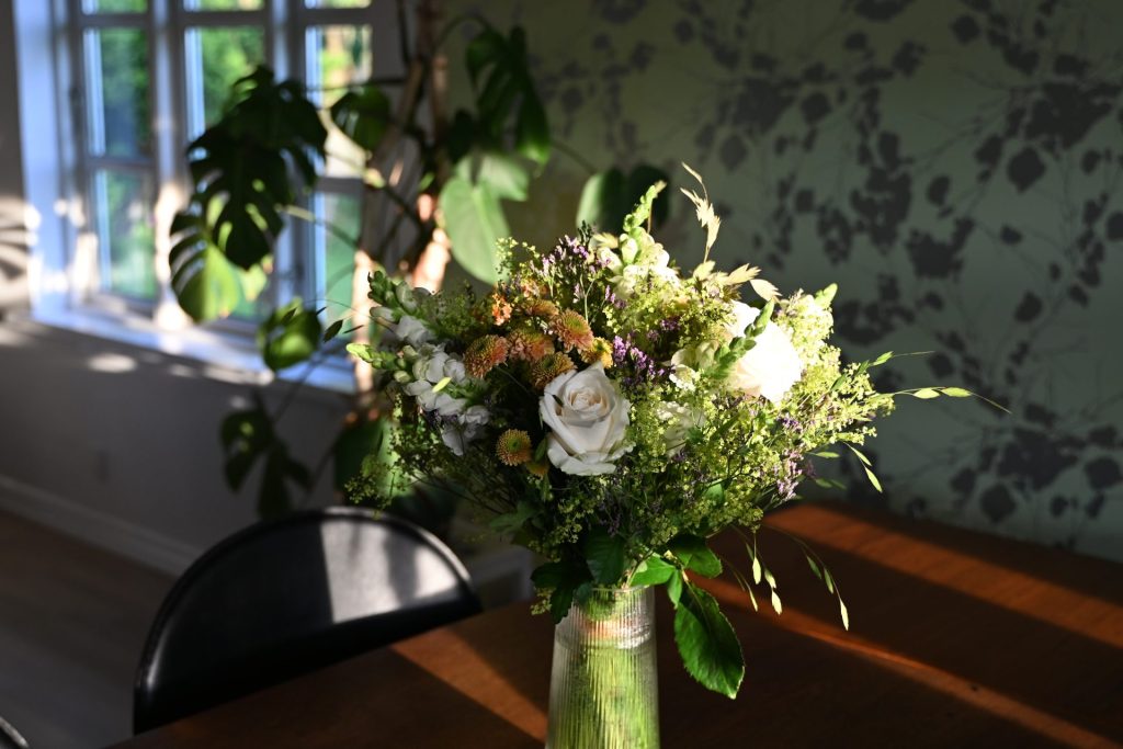 En smuk buket i en glasvase, der står i en stue. Aftensolen skinner på buketten ind gennem vinduet.