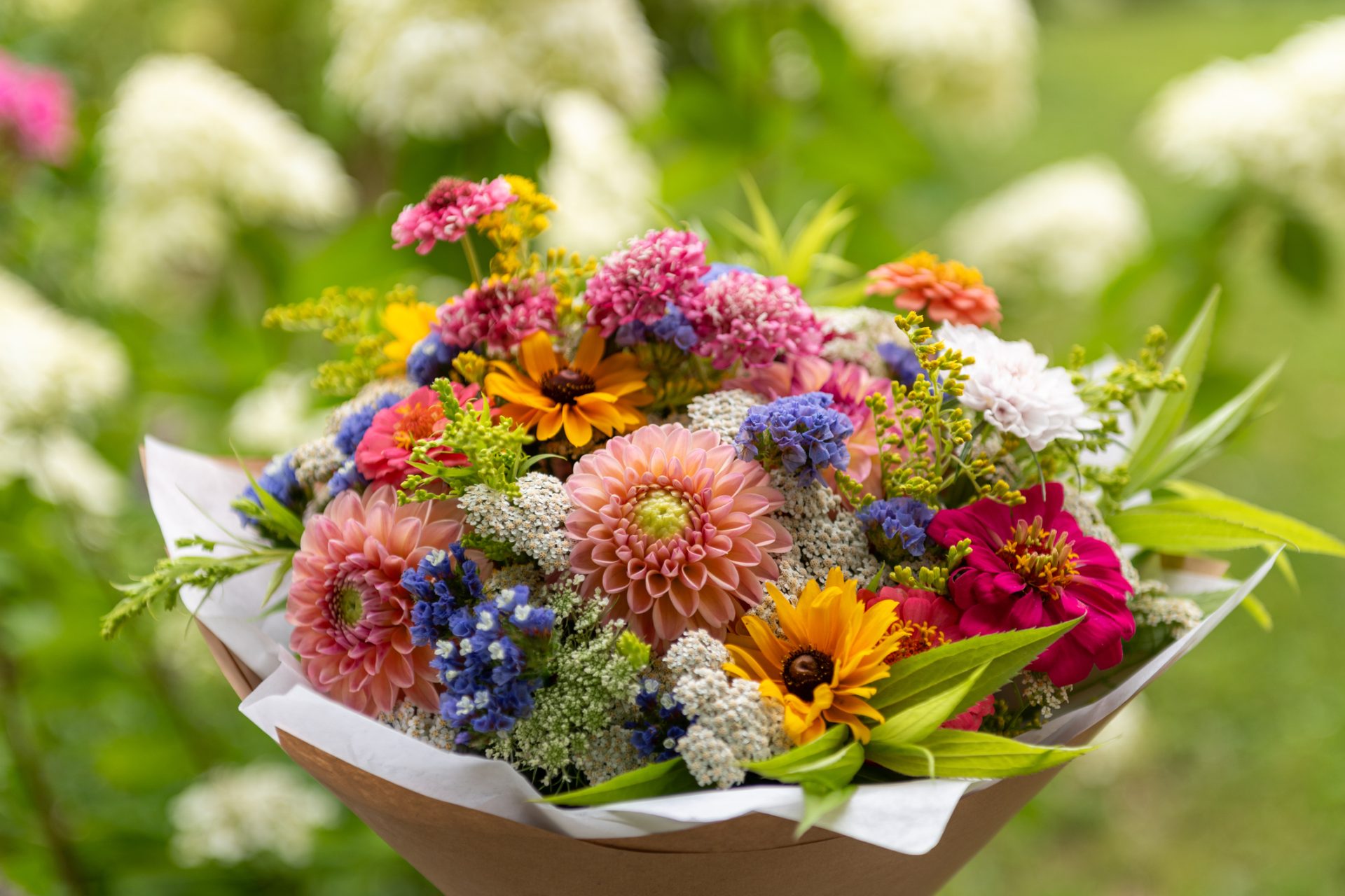 En smuk sommerbuket i blandede friske farver. BUketten er pakket fint i brunt papir og hvidt silkepapir.